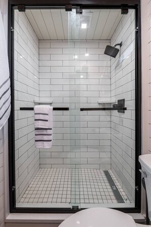 A glass-enclosed shower with white tiles, a towel rack, and a toilet visible through the glass.