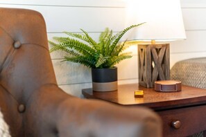 A brown leather armchair, a small wooden side table with a lamp, a potted fern, and a small object on the table. - Cozy Tiny Container Home-The Outwest (Waco)