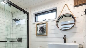 A modern bathroom with a glass shower enclosure, a white toilet, a sink with a mirror, and a framed picture on the wall.