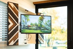 A flat-screen TV mounted on a wall with a geometric pattern, positioned in front of a window with blinds.