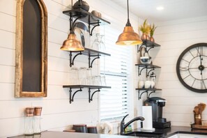 A kitchen with black metal shelves, hanging pendant lights, and a large wall clock. - The Newtonian Tiny Container Home near Magnolia (Waco)