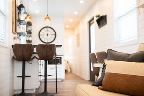 A modern interior with a sofa, two bar stools, a kitchen area, and pendant lighting. - The Newtonian Tiny Container Home near Magnolia (Waco)