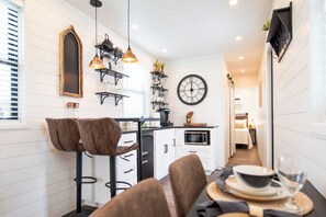 Una cocina estrecha con comedor, que incluye un reloj, luces colgantes y un taburete de bar.