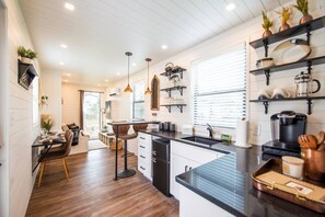 A modern kitchen with a central island, pendant lighting, and built-in shelves. - The Newtonian Tiny Container Home near Magnolia (Waco)