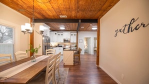 Una cocina moderna con armarios blancos, techo de madera y comedor con mesa y sillas de madera.
