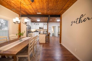 Une cuisine moderne avec des meubles blancs, un plafond en bois et un coin repas comprenant une table et des chaises en bois.