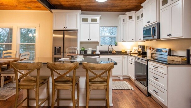 Una cocina moderna con armarios blancos, un refrigerador de acero inoxidable y techo de madera.