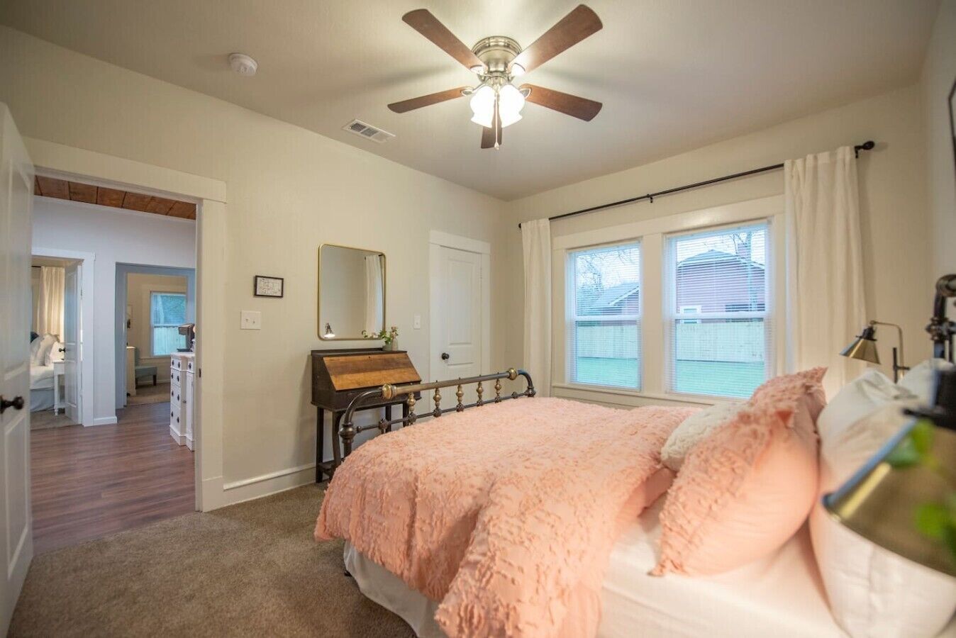 A bedroom with a bed, a ceiling fan, a dresser, a mirror, and a window.