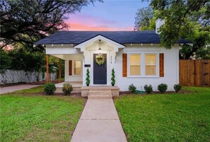 Une maison de plain-pied avec un porche à l’avant, une porte d’entrée sombre et un petit jardin devant.