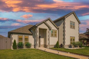 Two-story home with a gable roof and stucco exterior, featuring a covered porch and beautifully manicured lawn.