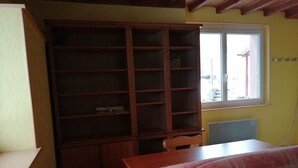 A room with a wooden bookshelf, a table, and a window. - Apartment in quiet house surrounded by meadows. (Cleurie)