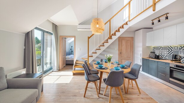 Eine moderne Küche mit Essbereich, einer Holztreppe und großen Fenstern.