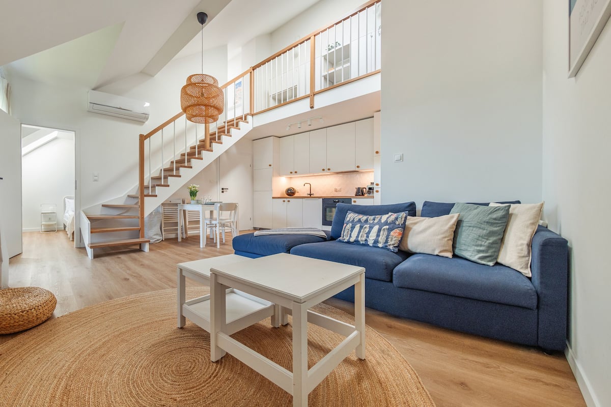 A spacious living area with a blue sofa, a white coffee table, and a wooden staircase leading to an upper level.