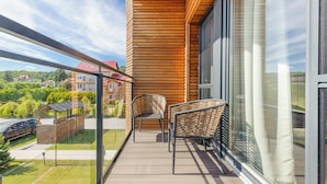 Ein Balkon mit Korbstühlen, Glasgeländer und Blick auf ein Wohngebiet.