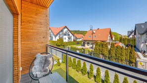 A balcony with a wooden exterior, a chair with a fur throw, and a view of residential buildings with red roofs. - Apartamenty Sun & Snow Nautikka Resort (Krynica Morska)