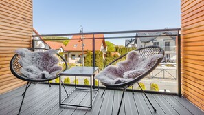 A balcony with two black wicker chairs and a small table, wooden walls, and a view of neighboring houses. - Apartamenty Sun & Snow Nautikka Resort (Krynica Morska)