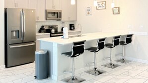Una cocina moderna con electrodomésticos de acero inoxidable, suelo de baldosas de mármol y una isla central con taburetes de bar.