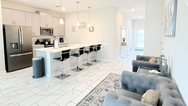 Una cocina moderna con armarios blancos, un refrigerador de acero inoxidable y una isla central con taburetes de bar.