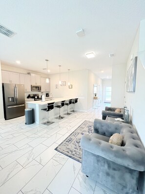 A modern kitchen with white cabinets, a stainless steel refrigerator, and a central island with bar stools. - Champions Gate, Family Fun Retreat | 5BR Pool Home (Four Corners)