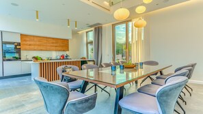 Un comedor moderno con una mesa de vidrio, sillas tapizadas en gris y vistas a la cocina y al exterior.
