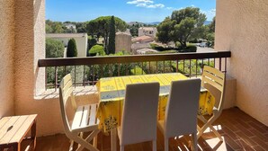Une terrasse extérieure couverte, avec une table et des chaises, donnant sur la ville et offrant une vue sur un ciel dégagé.