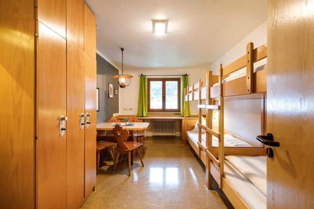 Et soveværelse med køjesenge i træ, et spisebord med stole, et vindue med grønne gardiner og en radiator under vinduet.