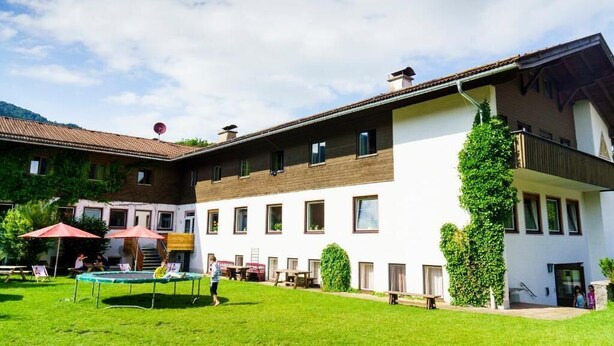 A two-story building with a courtyard, featuring a trampoline and outdoor seating area. - Jugendherberge Kreuth-Scharling - Hostel (Kreuth)