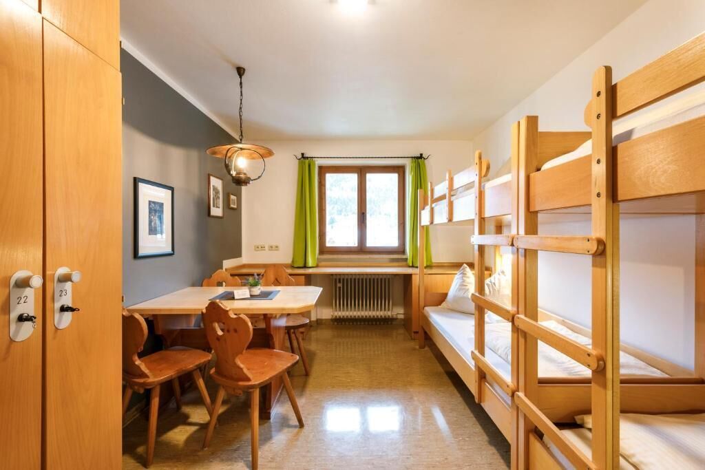 A compact room with bunk beds, a dining table with chairs, a radiator, and a window with curtains.