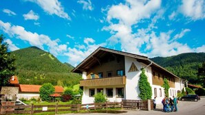 A two-story building with a sloped roof, a balcony, and a mountain backdrop.