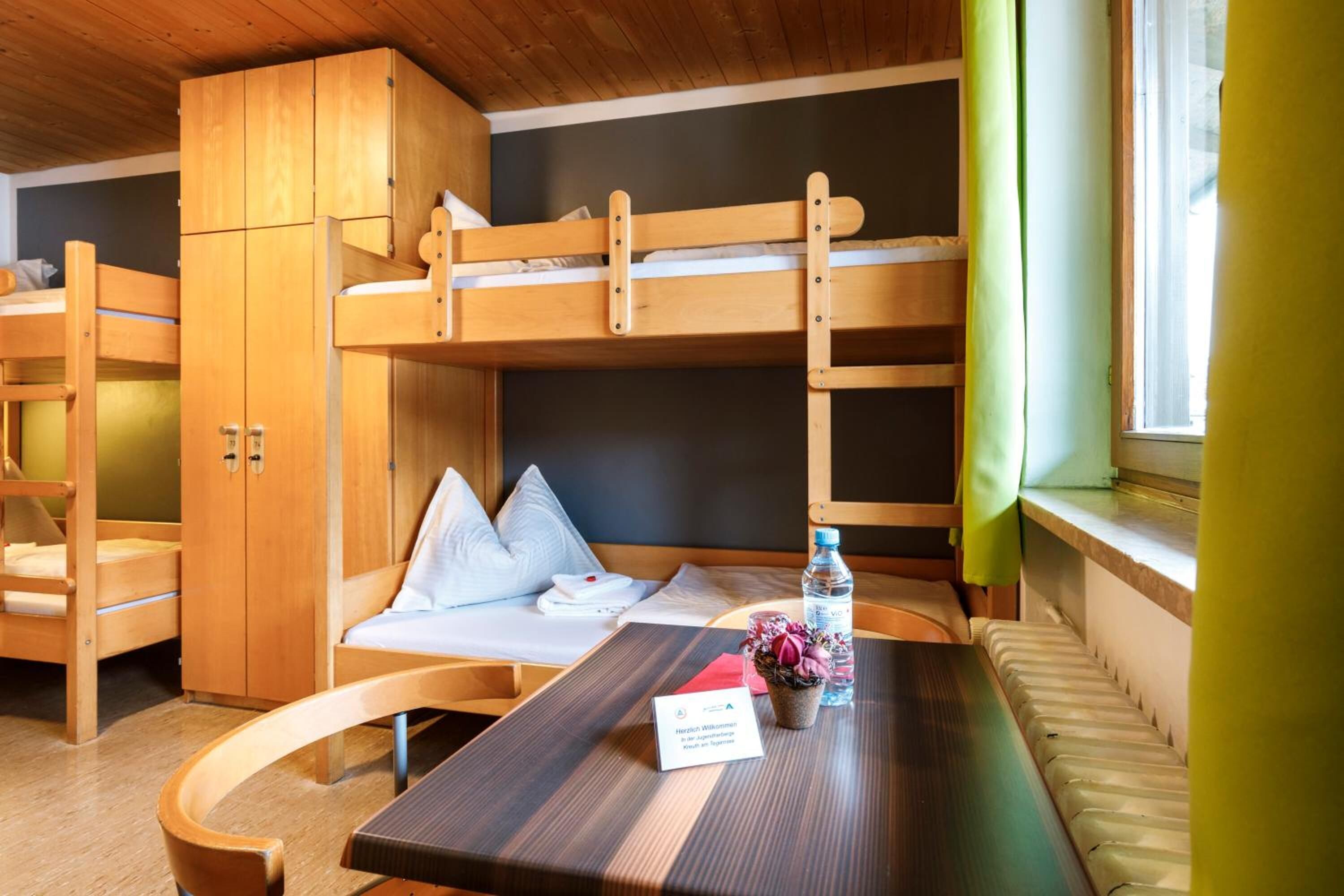 Habitación con literas, una mesa de madera, una planta pequeña y una botella de agua.