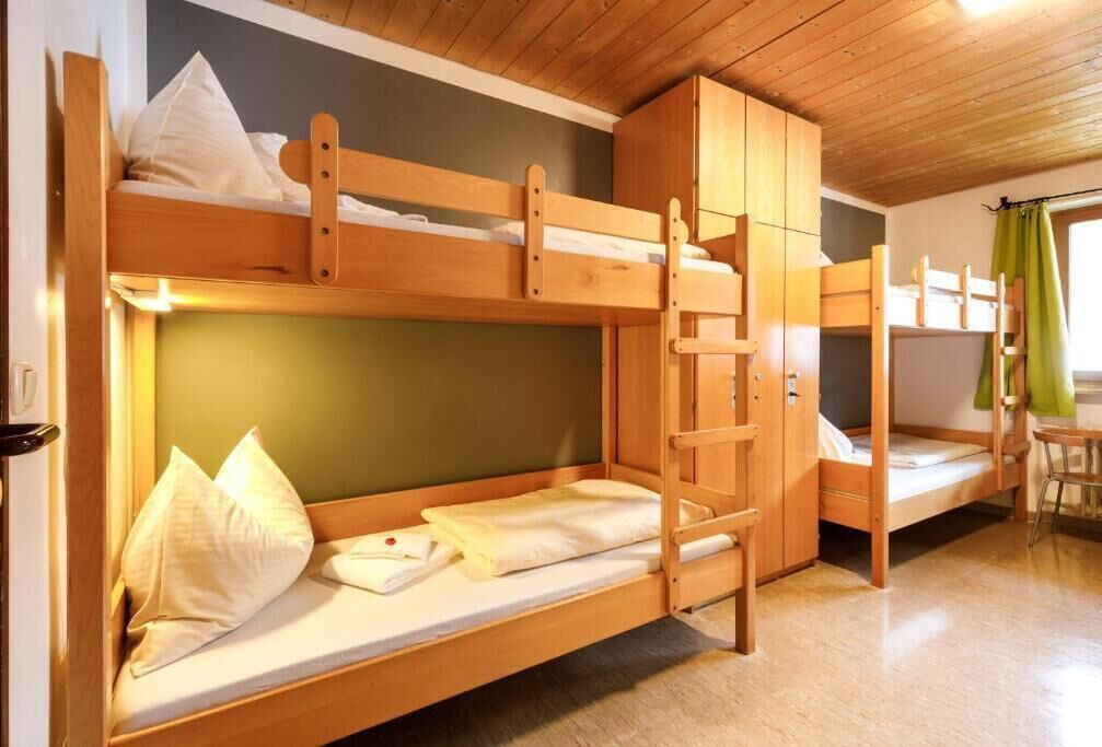 Een slaapkamer met een stapelbed, houten meubels, een groene wand en een raam met gordijnen.