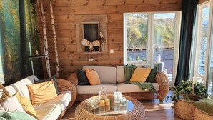 A cozy log cabin interior with a sofa, wicker coffee table, and large windows offering a view of the outdoors.