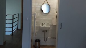 A bathroom with a white sink, mirror, and towel rack. There is a metal trash can and a wooden floor. The bathroom has a brick wall and a white door. - Villa Sorella Beautiful 3-bedroom Villa in Karanac (Knezevi Vinogradi)