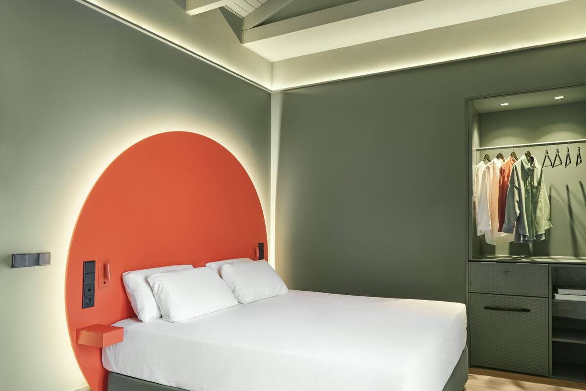 A modern bedroom with a bed, a circular accent wall, a wardrobe, and a mirror.
