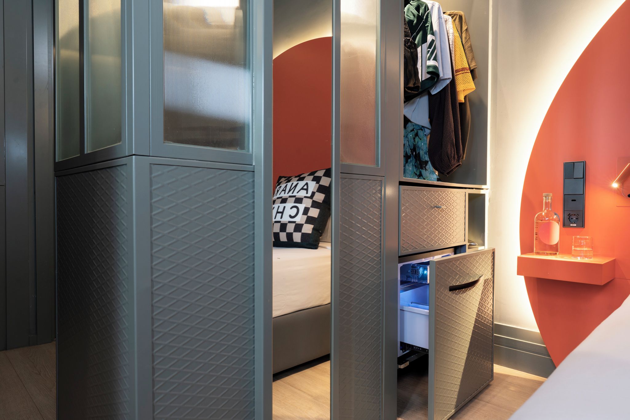 Une chambre à coucher moderne avec un lit, une armoire et une table de chevet sur laquelle se trouvent une bouteille et des verres.