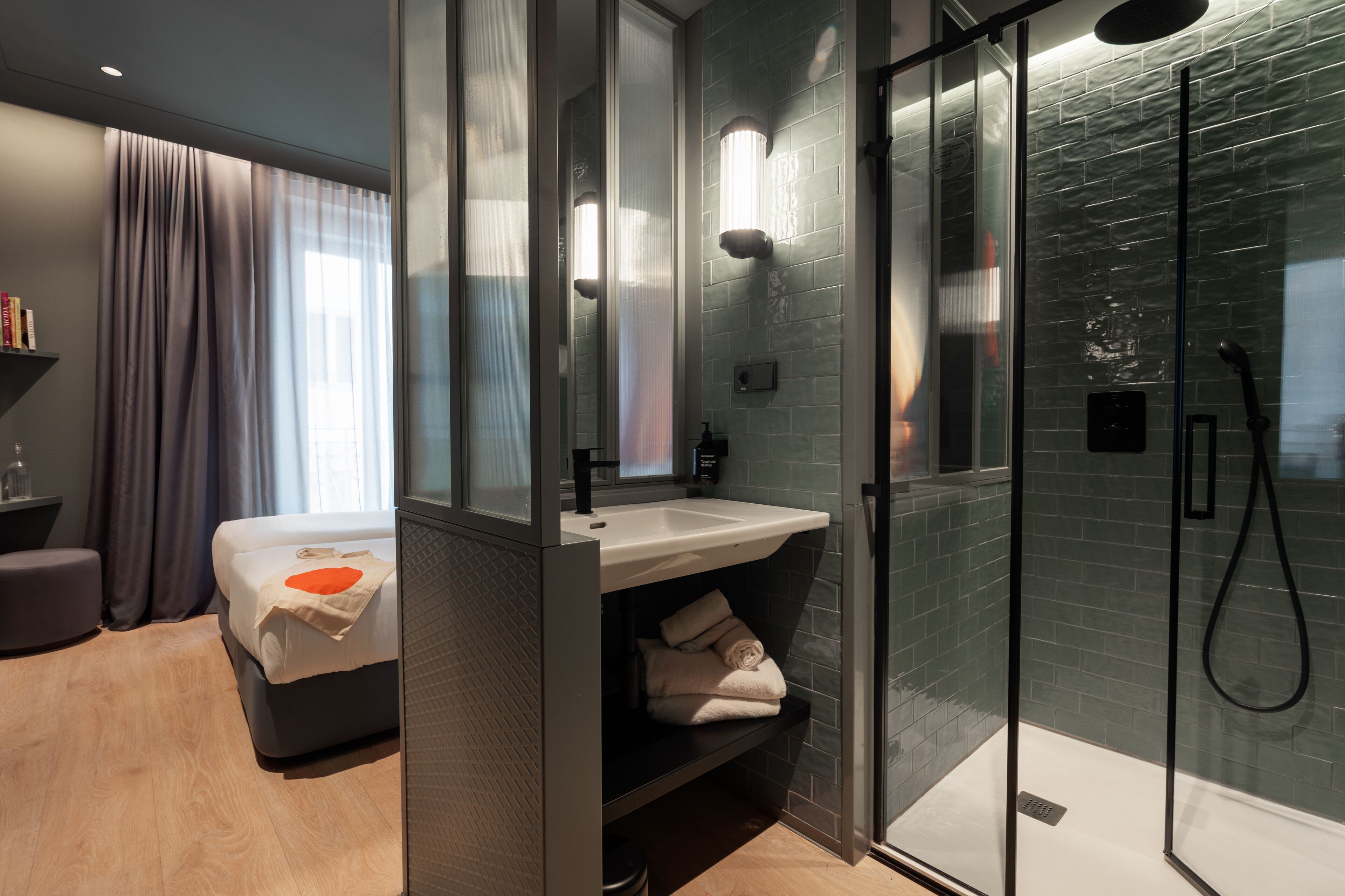 A modern bathroom with a glass shower enclosure, a built-in sink, and a bedside table with a towel.