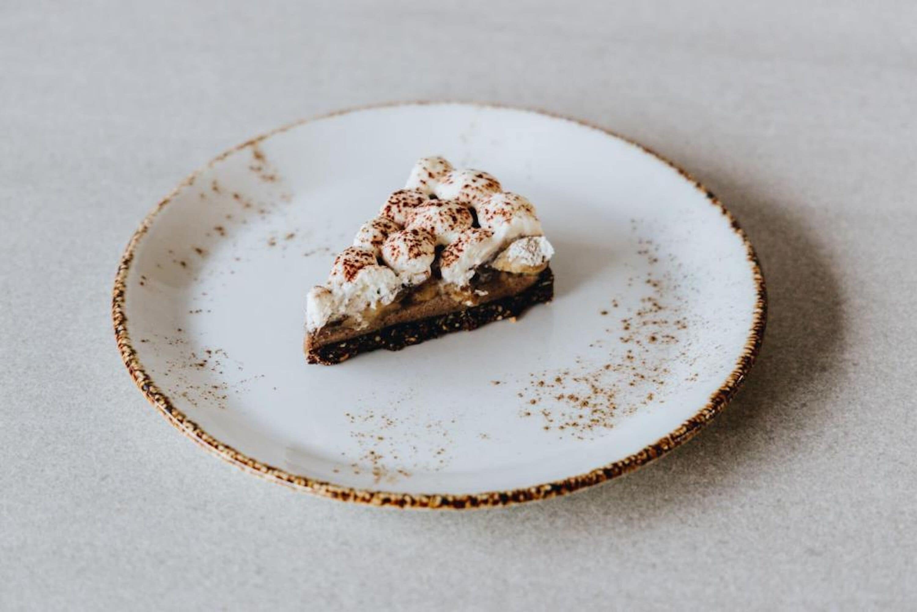 Una porción de pastel con crema batida y un poco de canela sobre un plato blanco.
