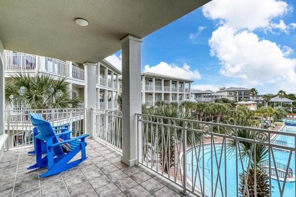 A balcony with blue Adirondack chairs, a pool, and a view of other buildings. - Newly Renovated Pool View Condo Near Beach & Rosemary | Lagoon Pool | 4 Bikes (Seacrest Beach)