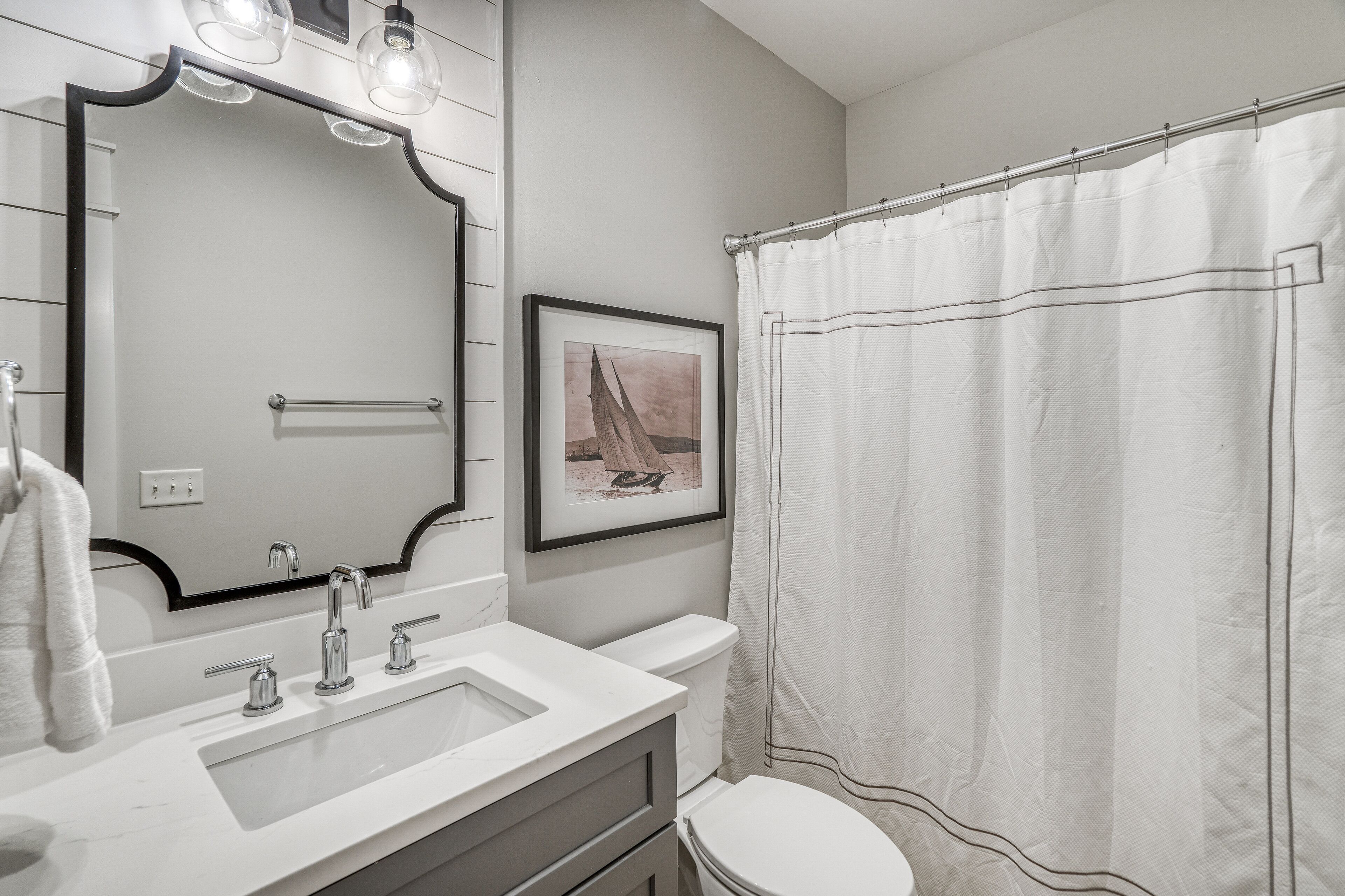 Un baño con un lavamanos blanco, un espejo con luces, un inodoro y una cortina de ducha.