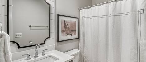 Un baño con un lavamanos blanco, un espejo con luces, un inodoro y una cortina de ducha.
