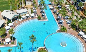 A large, curved swimming pool with multiple lanes, surrounded by palm trees and sun loungers. - Newly Renovated Pool View Condo Near Beach & Rosemary | Lagoon Pool | 4 Bikes (Seacrest Beach)