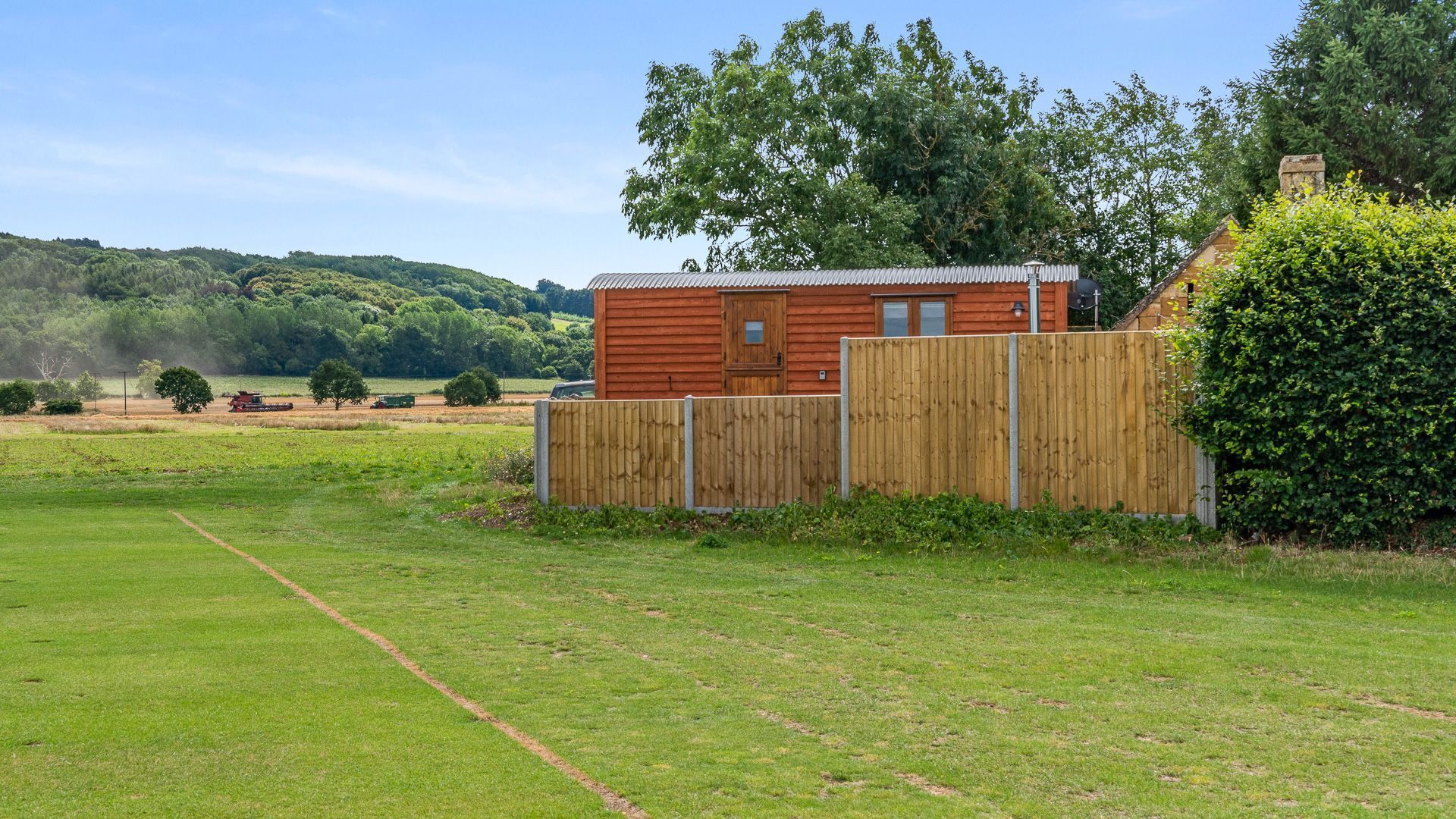 Une cabane en bois, surmontée d’un toit en métal, entourée d’une clôture en bois et d’une haie.