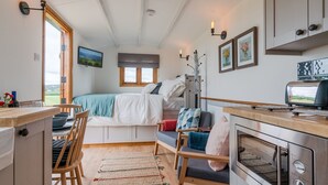 A compact, well-lit room with a bed, seating area, kitchenette, and a television. - Outbak Shepherds Hut - sleeps 2 guests  in 1 bedroom (Hailes)