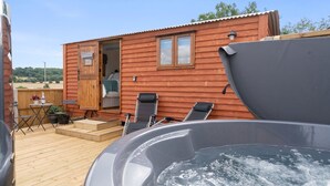A wooden cabin with a hot tub, outdoor seating, and a small deck. - Outbak Shepherds Hut - sleeps 2 guests  in 1 bedroom (Hailes)