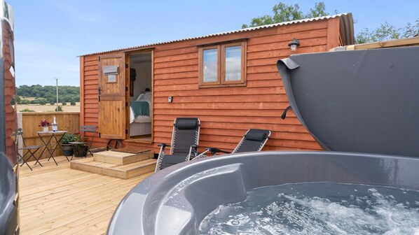 A wooden cabin with a hot tub, outdoor seating, and a small deck. - Outbak Shepherds Hut - sleeps 2 guests in 1 bedroom (Hailes)