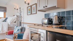 A compact kitchenette with a toaster, kettle, and oven, a small seating area with a chair and cushions, and a window with a view. - Outbak Shepherds Hut - sleeps 2 guests  in 1 bedroom (Hailes)