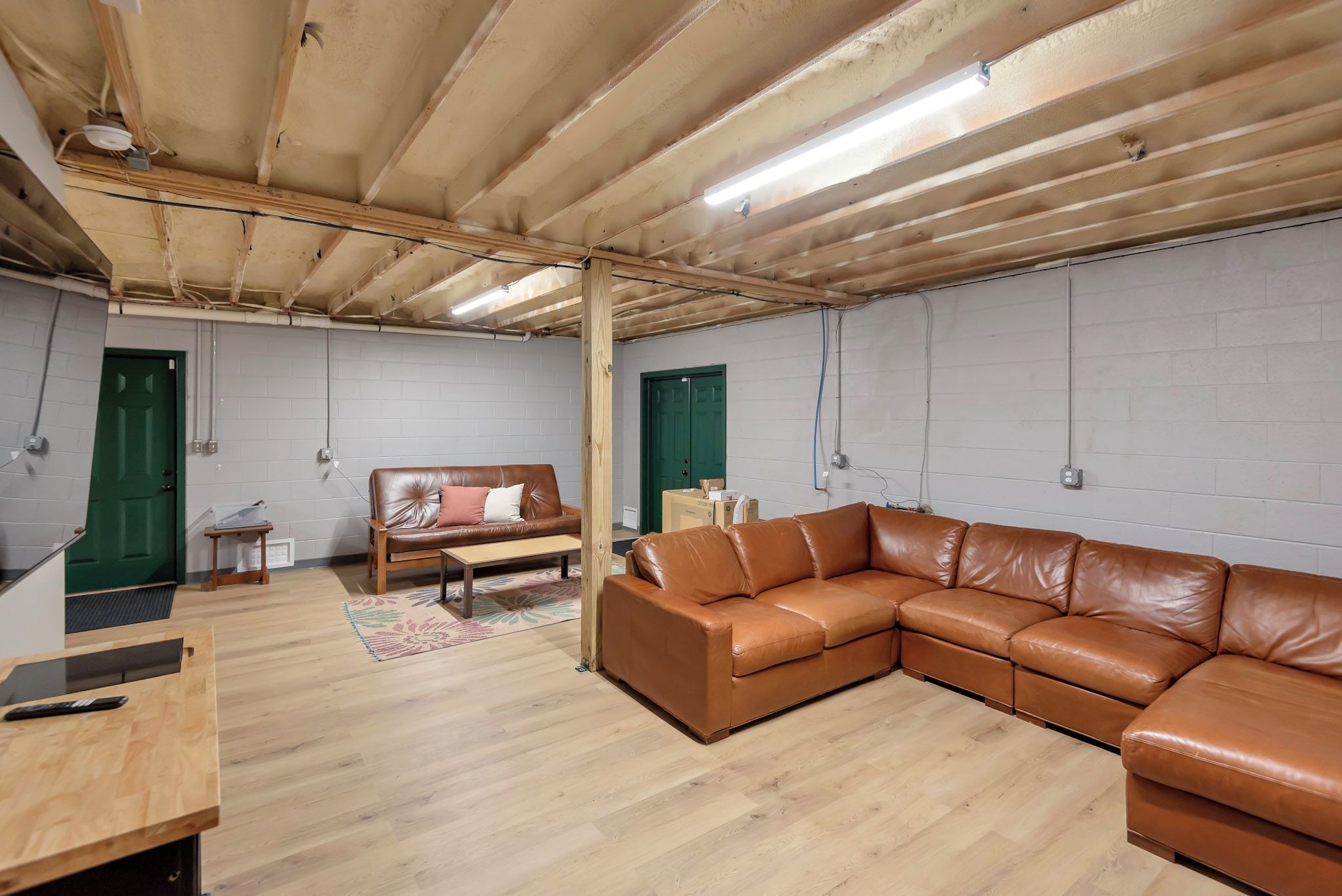 A spacious room with a wooden ceiling, a brown leather sofa, a wooden table, and a green door.
