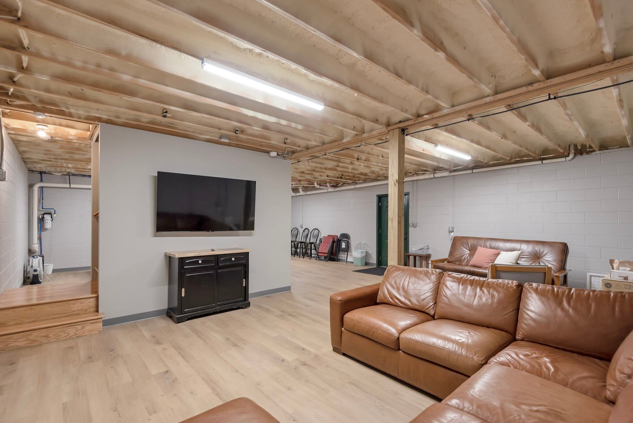 Un salón amplio con techo de madera, un televisor de pantalla plana montado en la pared, un sofá de cuero y una cafetera.