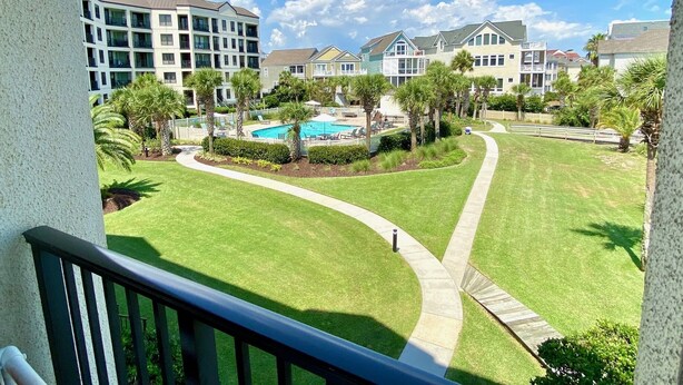 A residential area with a swimming pool surrounded by well-maintained lawns and palm trees. - Summer House 202 by Deserving Vacations (Isle of Palms)