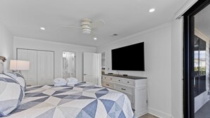 A bedroom with a bed, a dresser, a television, and a sliding glass door. - Summer House 202 by Deserving Vacations (Isle of Palms)